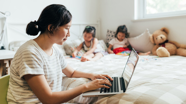 single mom on computer with kids on the bed